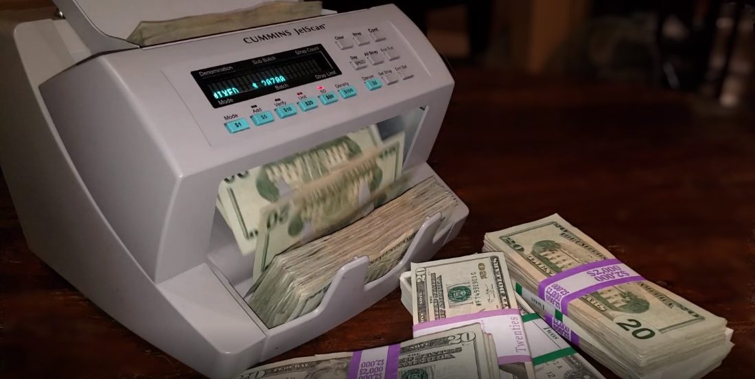 Cummins JetScan currency counter counting a stack of bills next to banded straps of cash